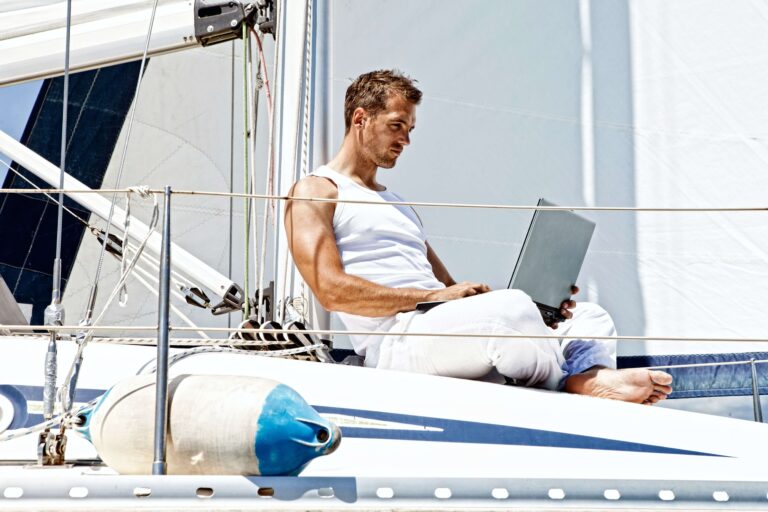 Hommes habillé en blanc avec ordinateur sur les jambes qui travaille sur un bateau et qui recharge ses batteries